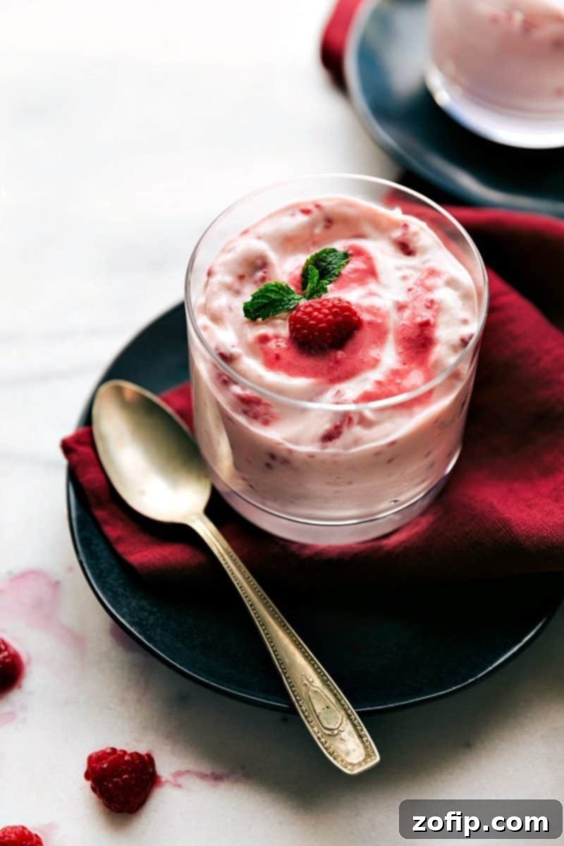 A close-up shot of the creamy Raspberry Fluff perfectly served in a clear glass cup, with a spoon resting invitingly on the side, highlighting its smooth, airy texture and vibrant pink color, inviting a delicious taste.