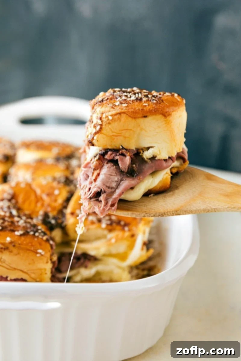 French Dip Sliders French Dip sandwiches fresh out of the oven with a spatula pulling one out.