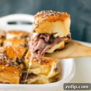 Warm Roast Beef Dippers 2 French Dip sandwiches fresh out of the oven with a spatula pulling one out.