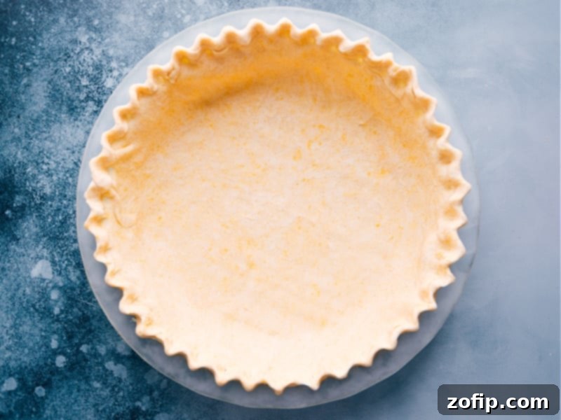 A pristine, homemade pie crust nestled in a clear glass pie dish, perfectly crimped and ready to be filled and baked to golden perfection for the ultimate Pumpkin Pecan Pie.