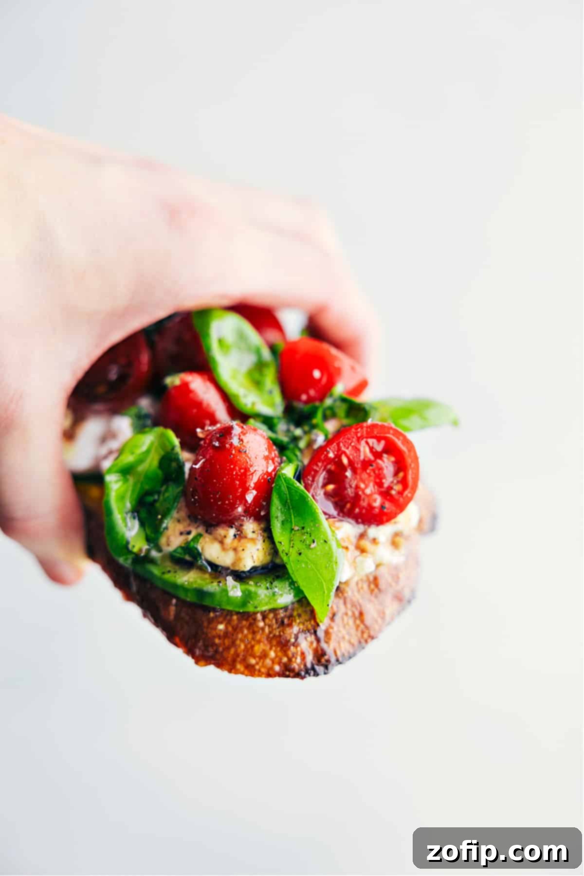 A hand holding a piece of Caprese Cottage Cheese Toast, showcasing all the vibrant and delicious toppings, ready to be eaten.