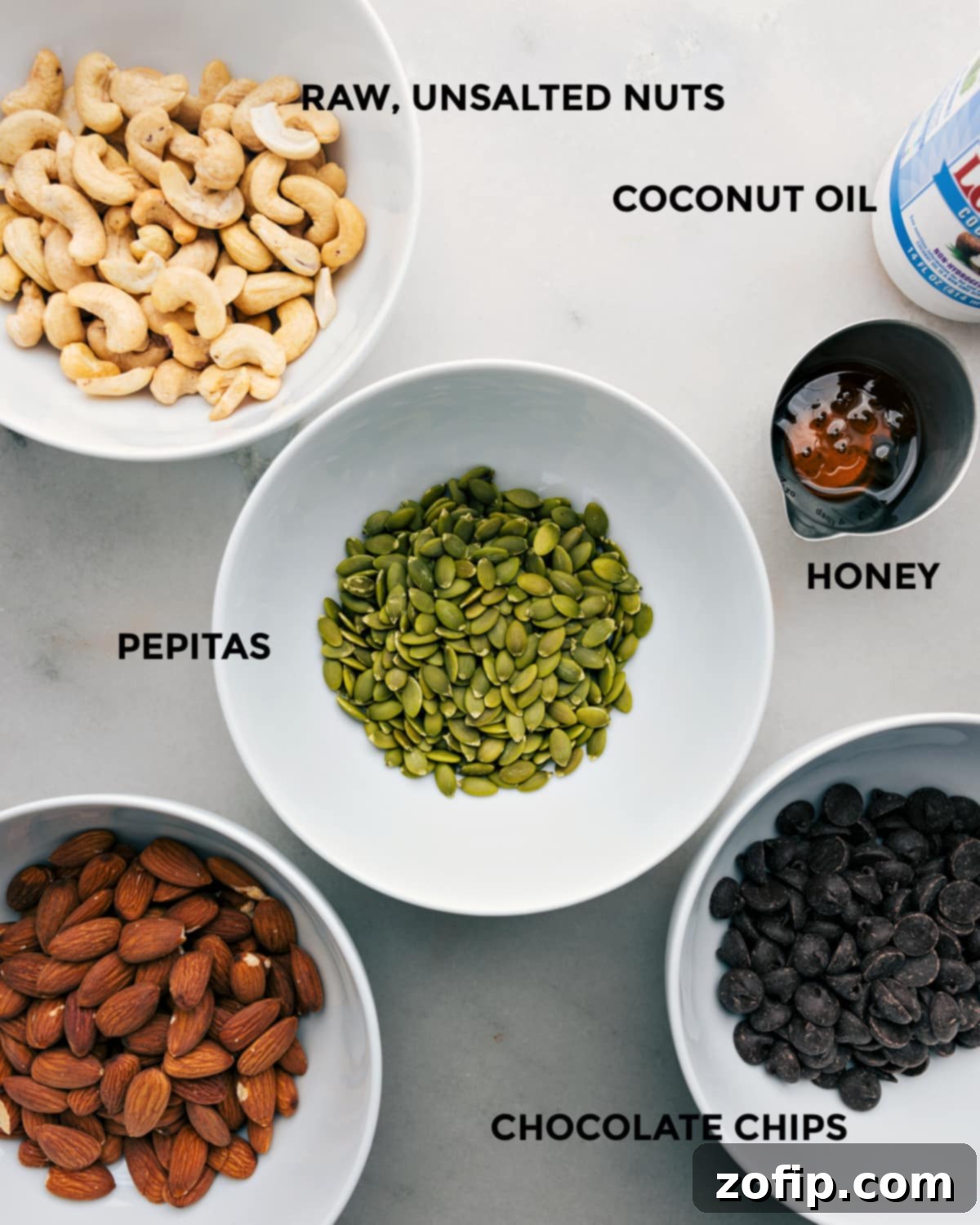 All the ingredients in this recipe like nuts, coconut oil, pepitas, honey, and chocolate chips prepped out for easy assembly.