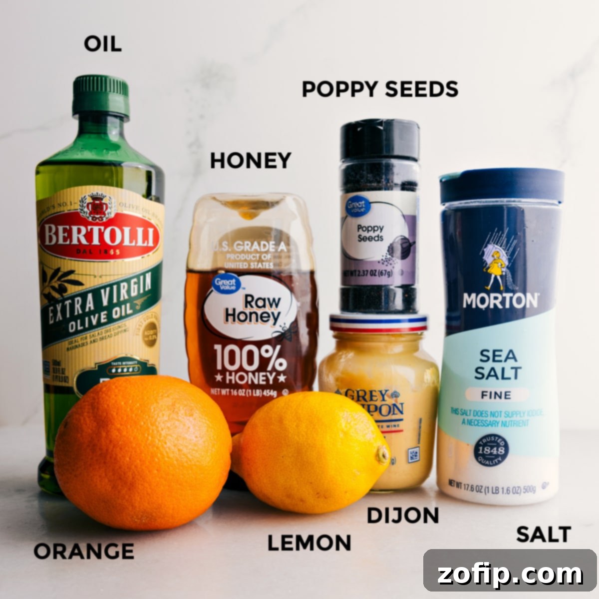 All dressing ingredients for mandarin orange salad laid out: olive oil, honey, poppy seeds, salt, Dijon mustard, a whole lemon, and a whole orange.
