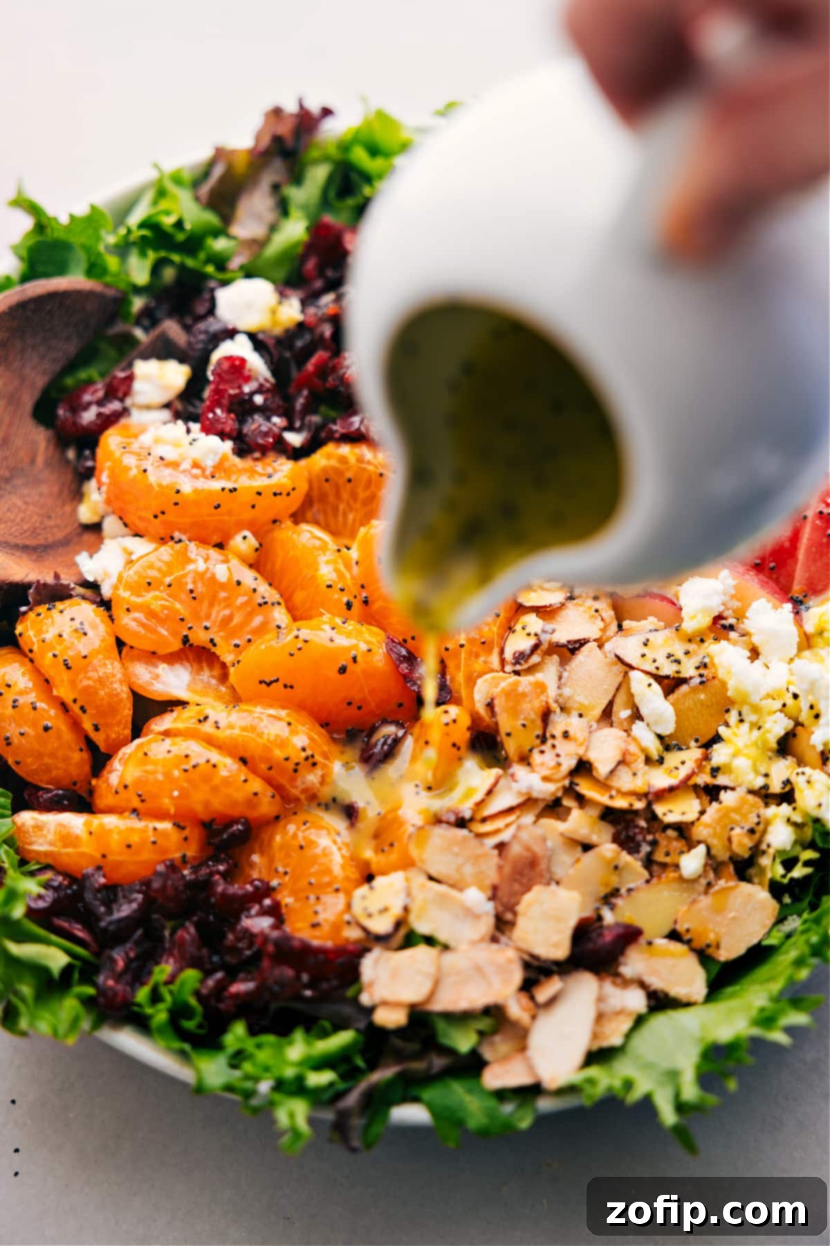 The vibrant mandarin orange salad in a bowl, with the citrus poppy seed dressing being drizzled generously over the top just before tossing and serving.