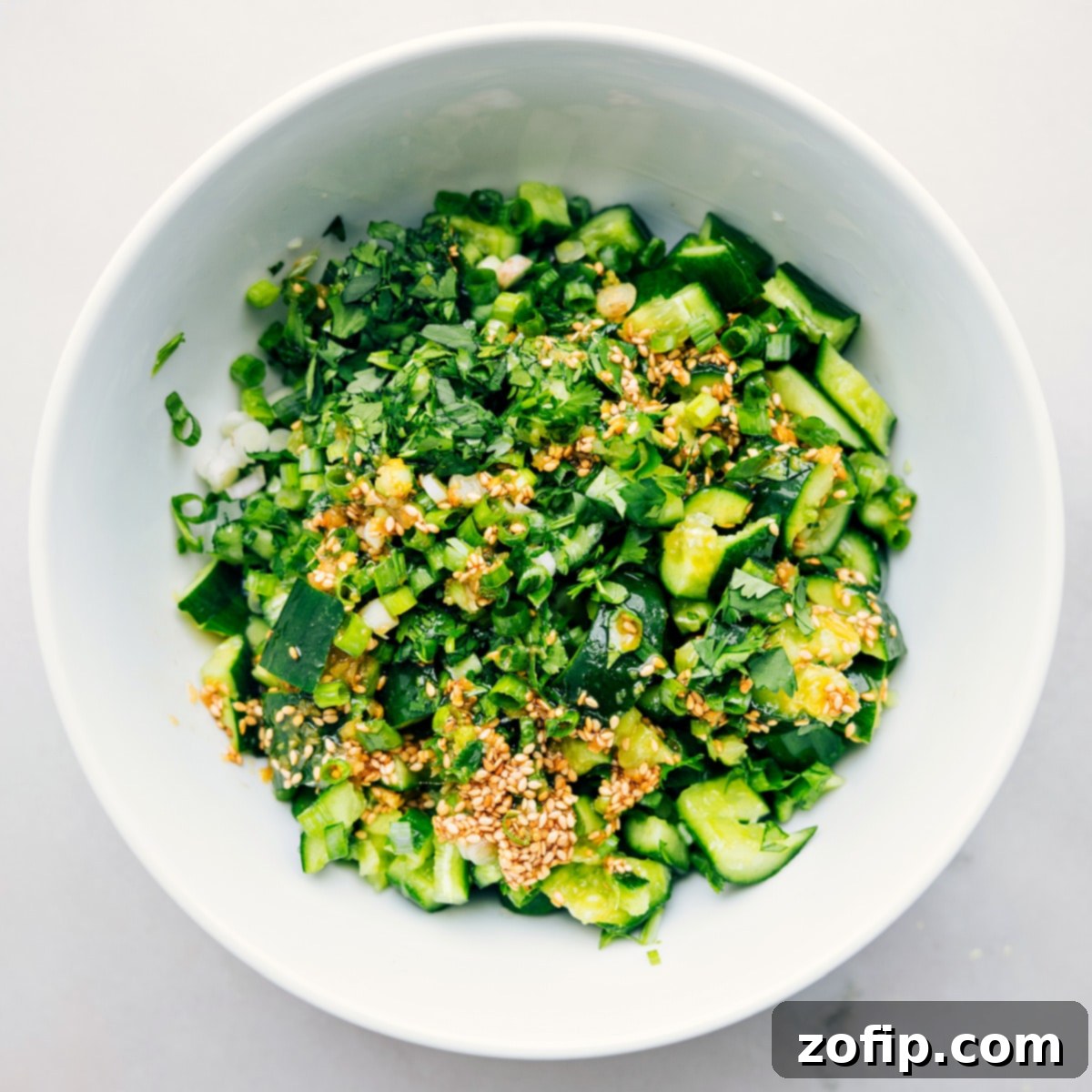 Assembling the Flavorful Smashed Cucumber Salad Smashed Cucumber Salad in a large mixing bowl with all ingredients, including dressing and fresh herbs, ready to be tossed together for a perfect blend of flavors.