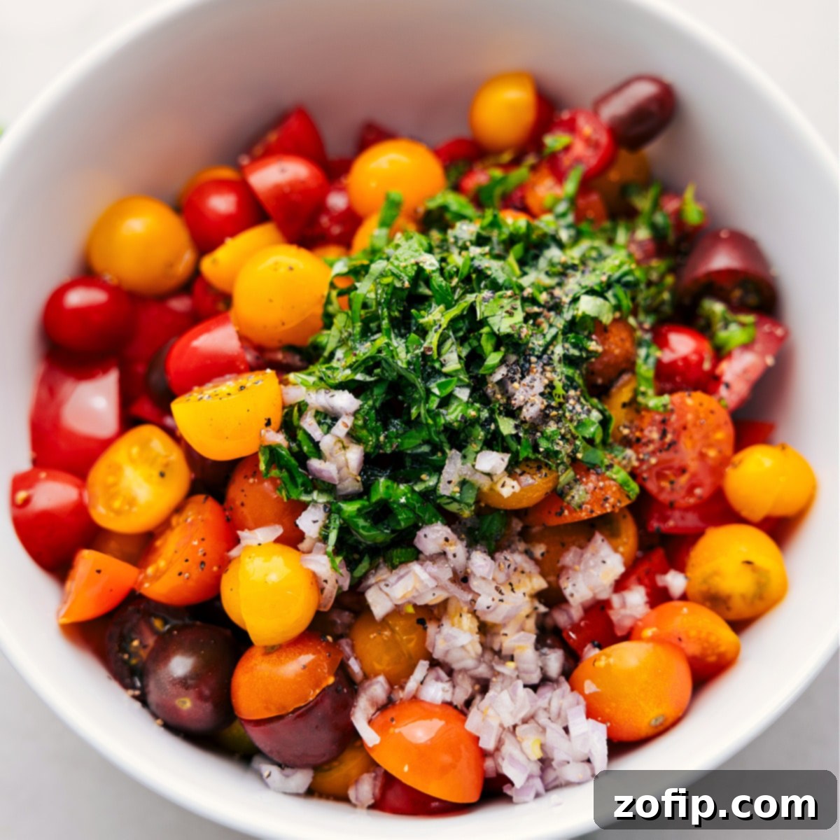All the prepared ingredients for the tomato salad are combined in a large bowl, ready to be gently tossed.
