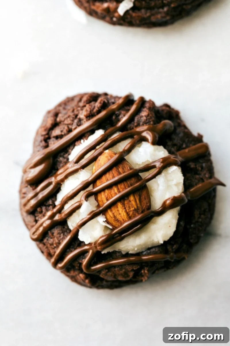 Up close overhead image of an Almond Joy Cookie showing a rich brownie base, creamy white coconut frosting, a whole roasted almond, and delicate chocolate drizzle.
