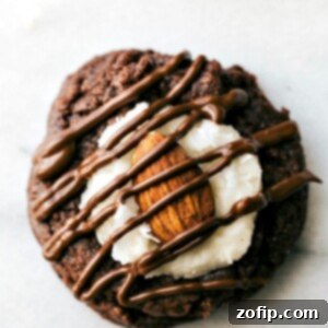 A delicious Almond Joy Cookie with a fudgy brownie base, creamy coconut frosting, a whole roasted almond, and elegant chocolate drizzle.