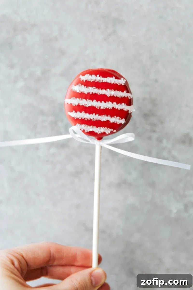 Image of a festive Candy Cane Oreo Pop, decorated with white stripes and sparkling sugar.