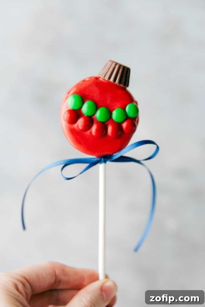 Ornament Oreo Pop: a colorful Christmas dessert Close-up image of a vibrant red Ornament Oreo Pop decorated with colorful M&M's and topped with a mini Reese's cup.