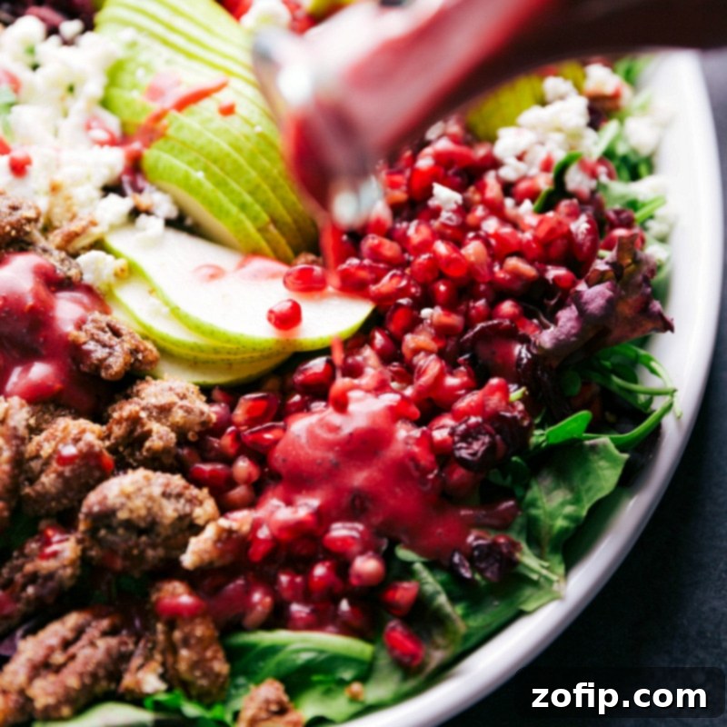 Preparing Raspberry Poppy Seed Dressing for Salad Homemade raspberry poppy seed dressing being poured over the fresh pomegranate arils, ready to be tossed with the salad, enhancing its vibrant flavors.