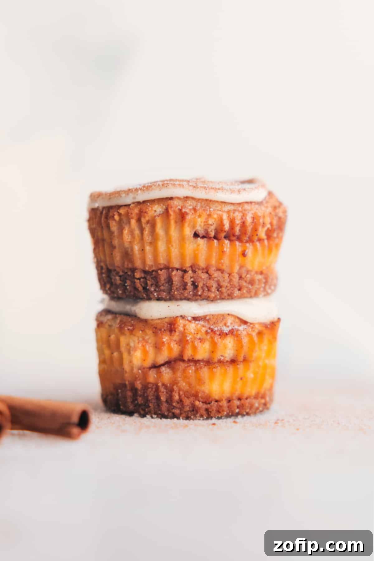 Stacked Mini Cinnamon Roll Cheesecakes topped with generous cream cheese frosting swirls, showcasing their perfect golden crust and creamy texture.