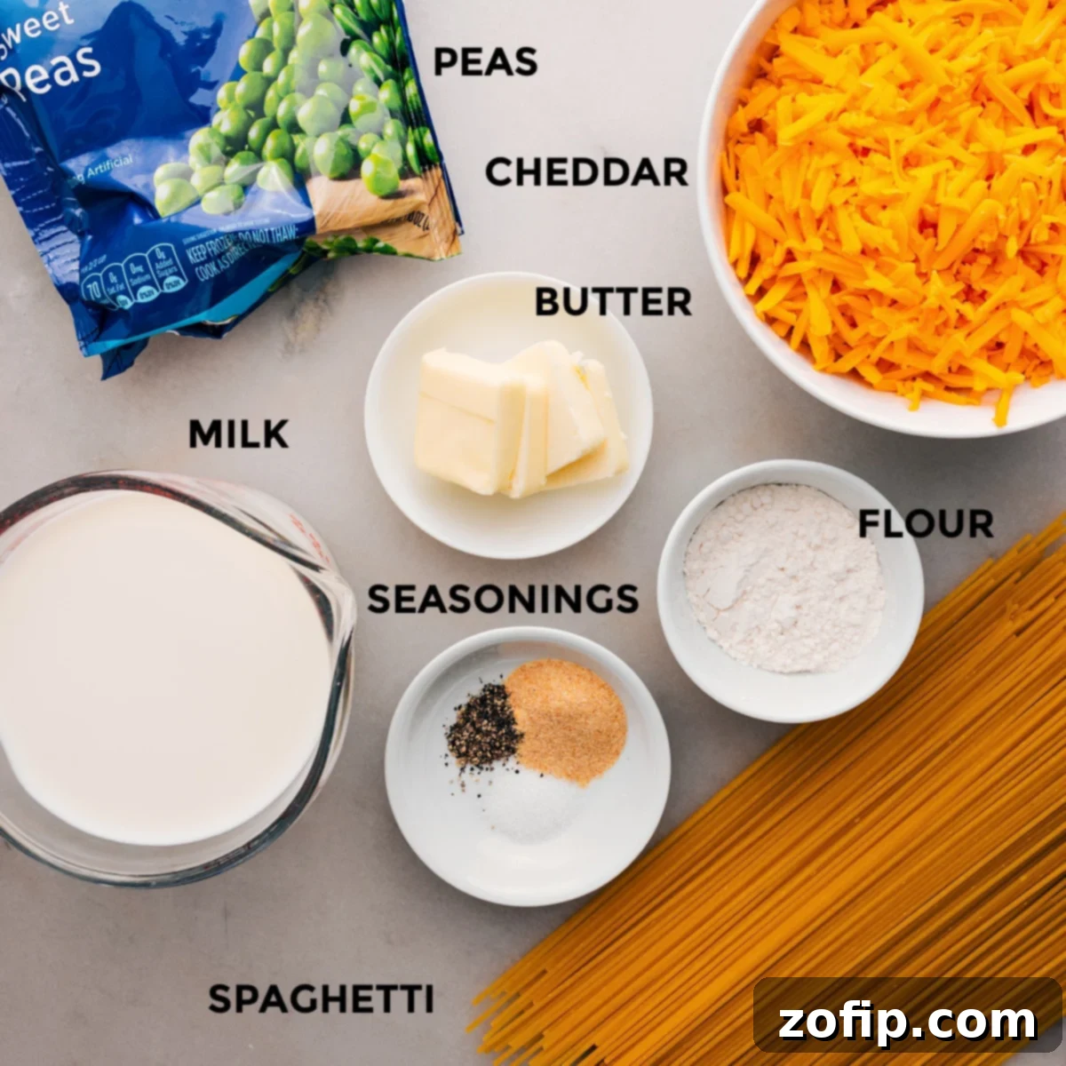 Ingredients In Cheesy Spaghetti All the fresh ingredients laid out for making cheesy spaghetti: pasta, flour, cheese block, butter, frozen peas, and a bottle of milk.