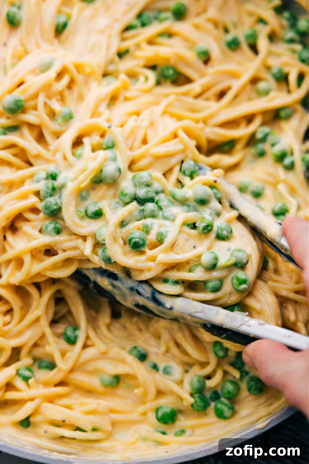 The Absolute Best Cheesy Spaghetti Recipe A close-up shot of a serving of cheesy spaghetti with green peas, topped with grated Parmesan cheese, glistening and ready to eat.