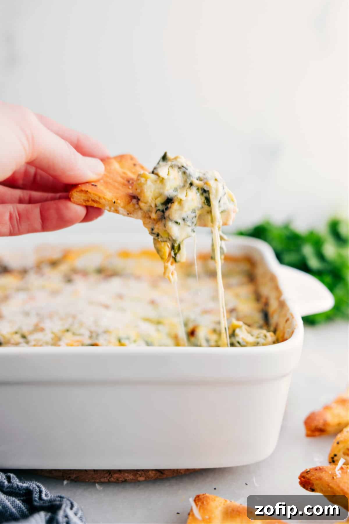 A big scoop of warm, cheesy Spinach Artichoke Dip rests on a crisp cracker, ready to be enjoyed.