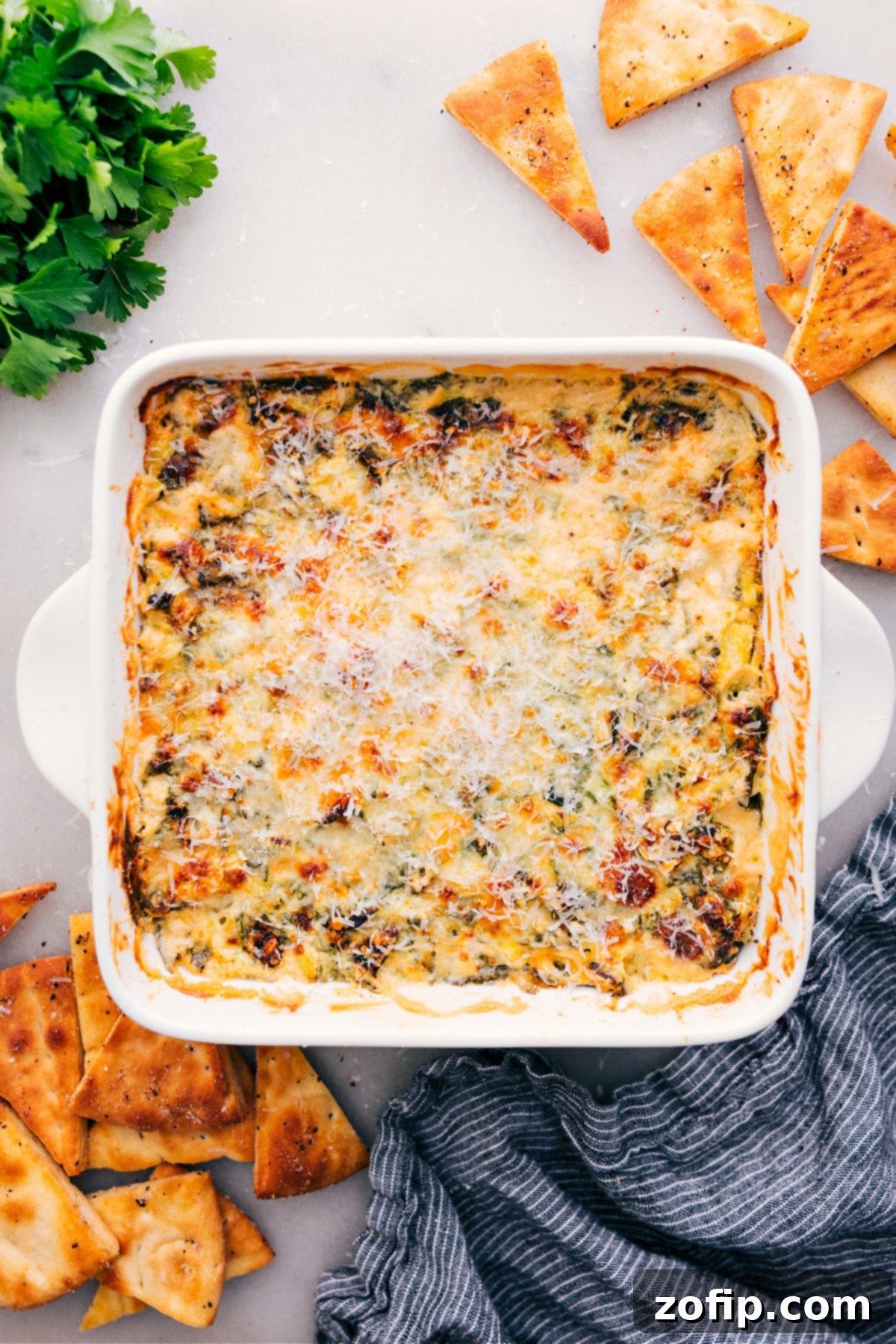 The ultimate party appetizer, Spinach Artichoke Dip, is freshly baked, hot, bubbly, and adorned with a golden-brown cheesy crust, ready to be served and savored.