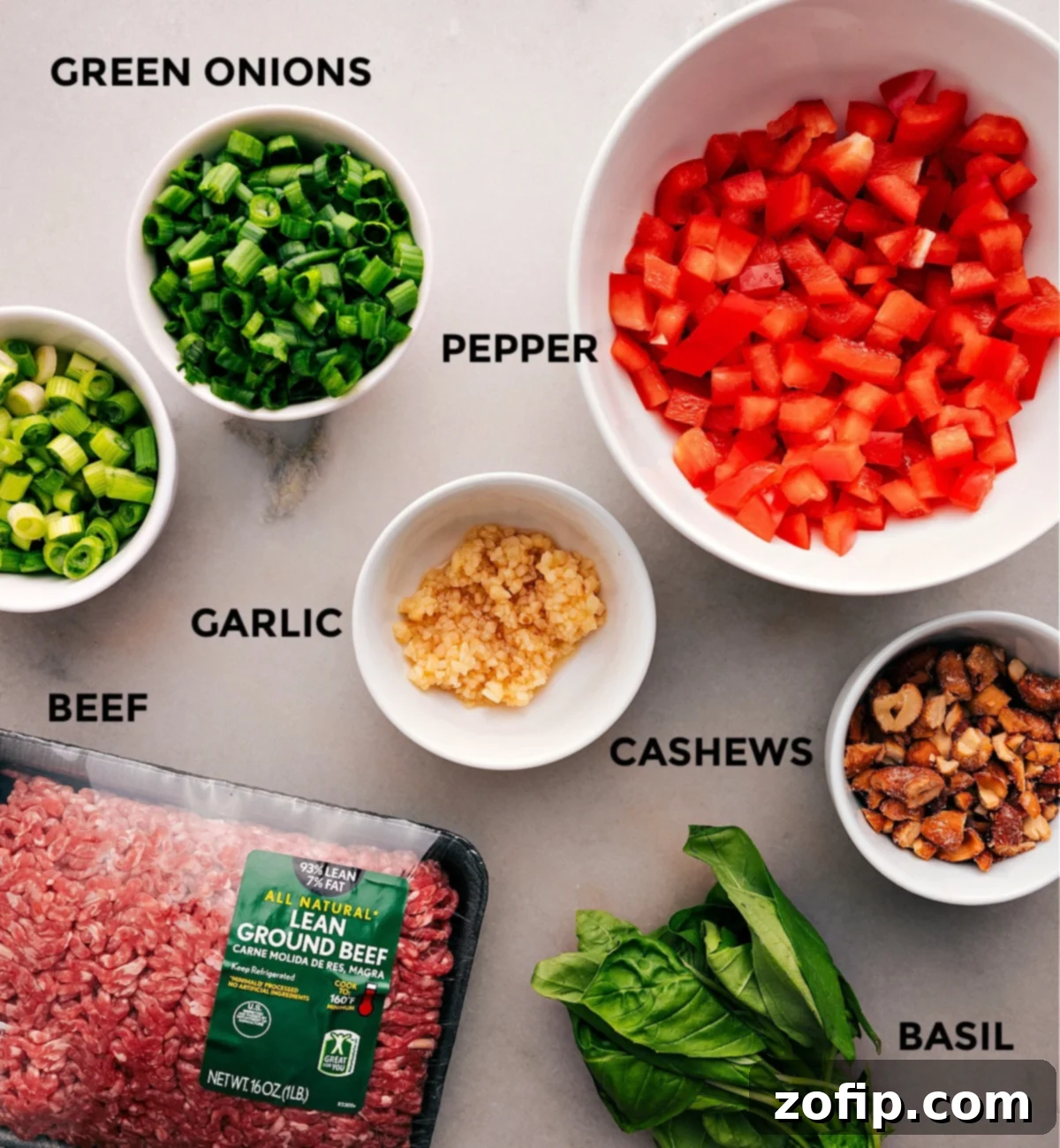 A collection of fresh ingredients for Asian Ground Beef, including colorful bell peppers, aromatic garlic, lean ground beef, crunchy cashews, and fragrant basil, all prepped and ready for cooking.
