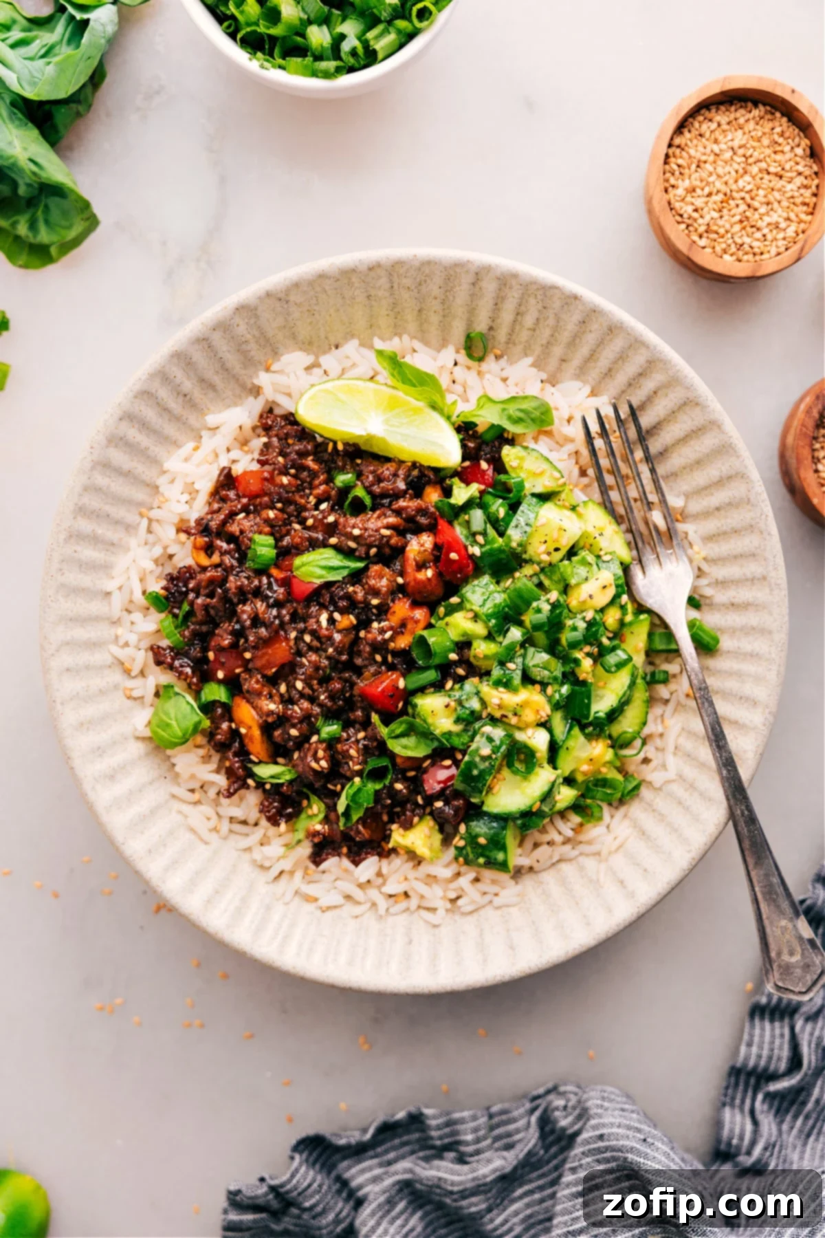 A beautifully plated dish of Asian Ground Beef served over white rice, accompanied by a vibrant and fresh cucumber avocado salad on the side.