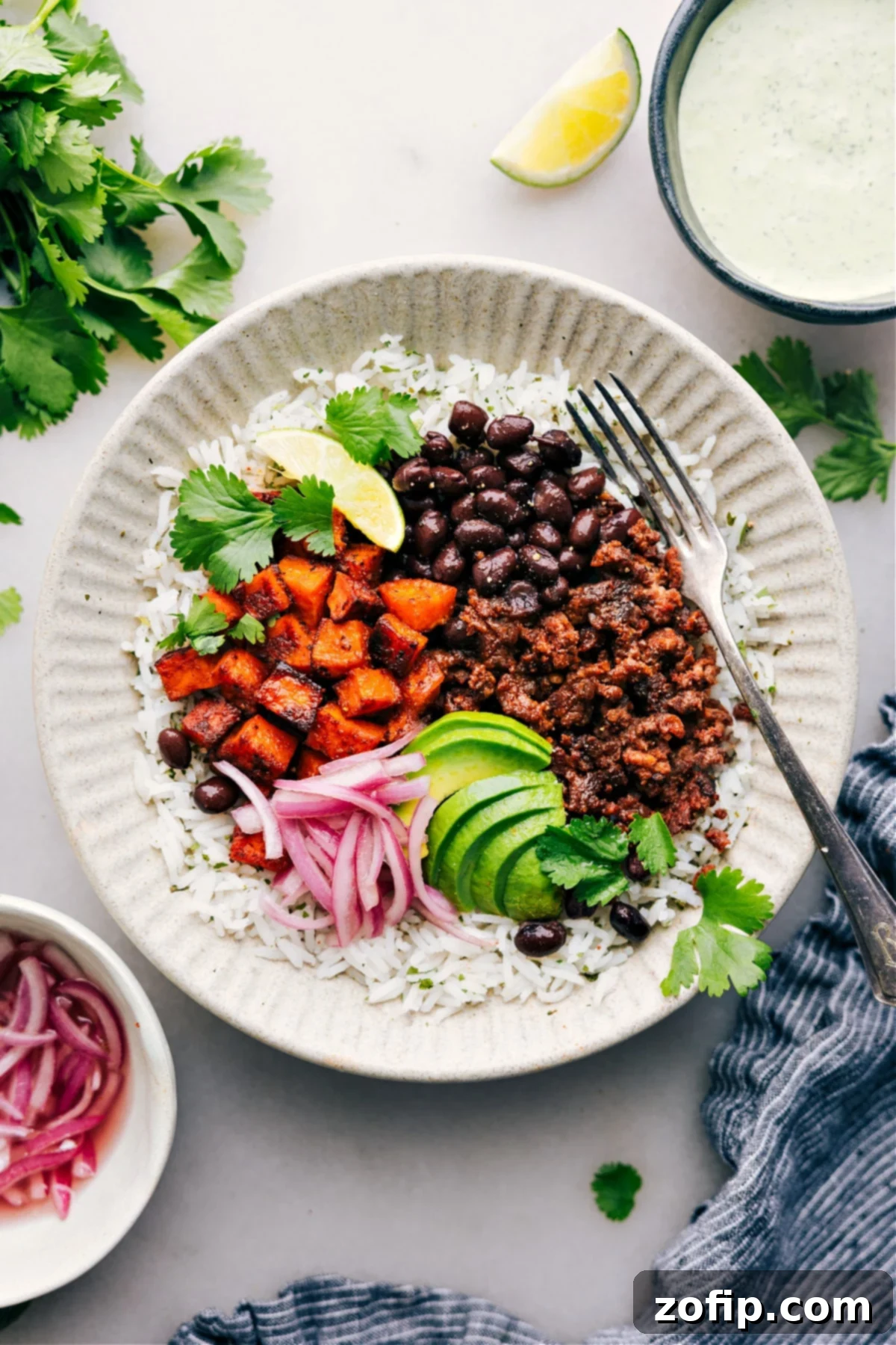 A vibrant Beef Burrito Bowl with fluffy rice, creamy avocado, crisp red onions, and fresh cilantro, drizzled with cilantro-lime sauce.