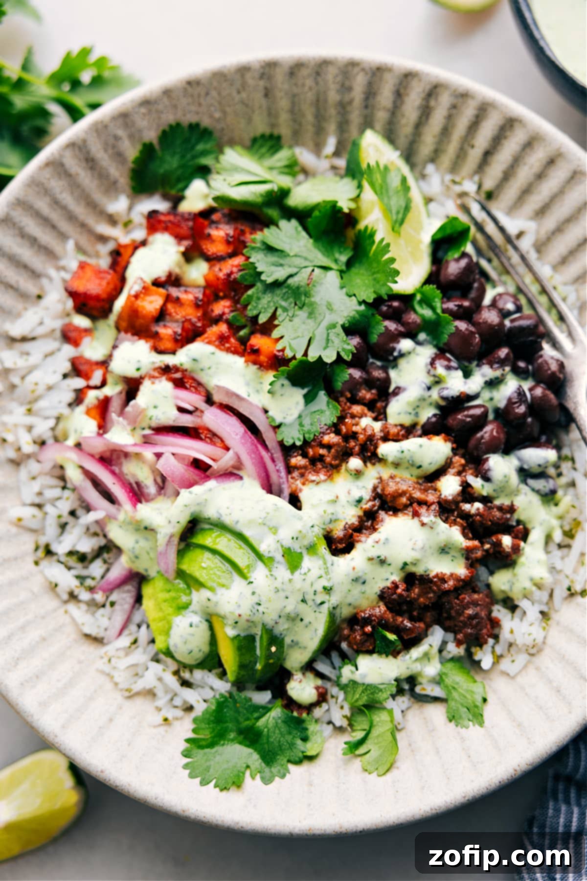 A perfectly assembled Beef Burrito Bowl recipe, generously drizzled with creamy cilantro-lime sauce, ready for a satisfying meal.