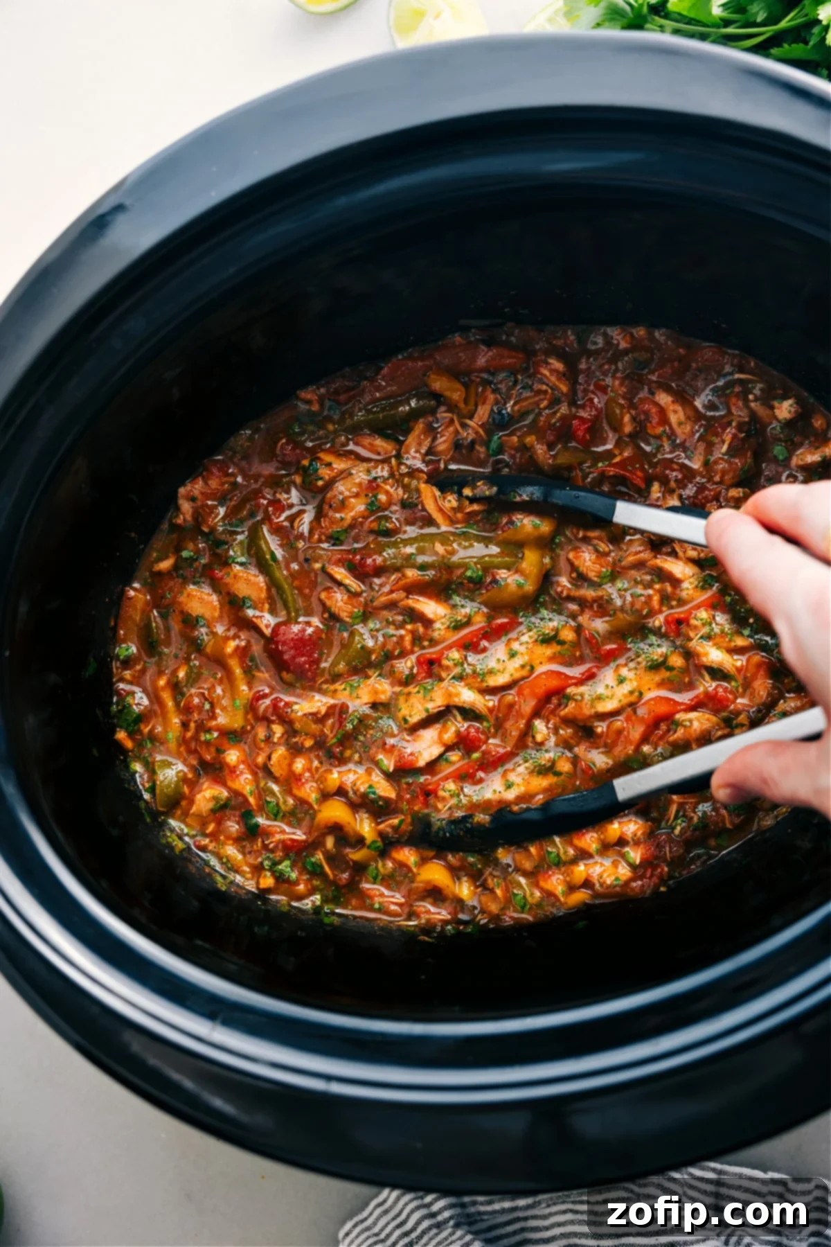 Flavorful Crockpot Chicken Fajitas with tender chicken, onions, and peppers, ready to be served from the slow cooker with tongs.