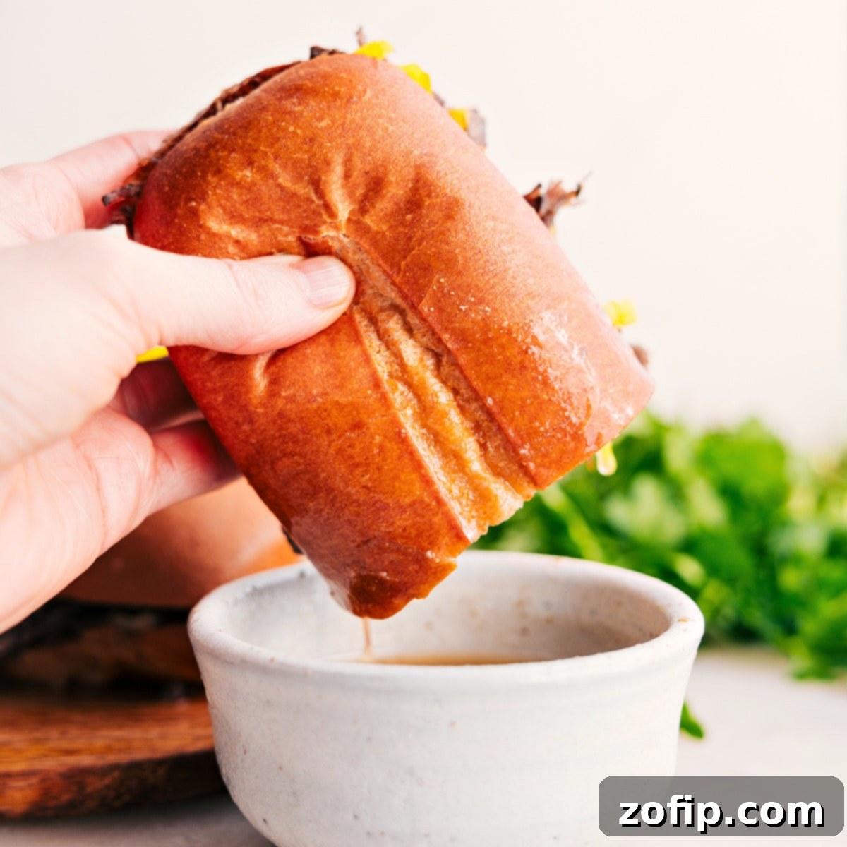 An Italian beef sandwich dipping into the broth from the crockpot.