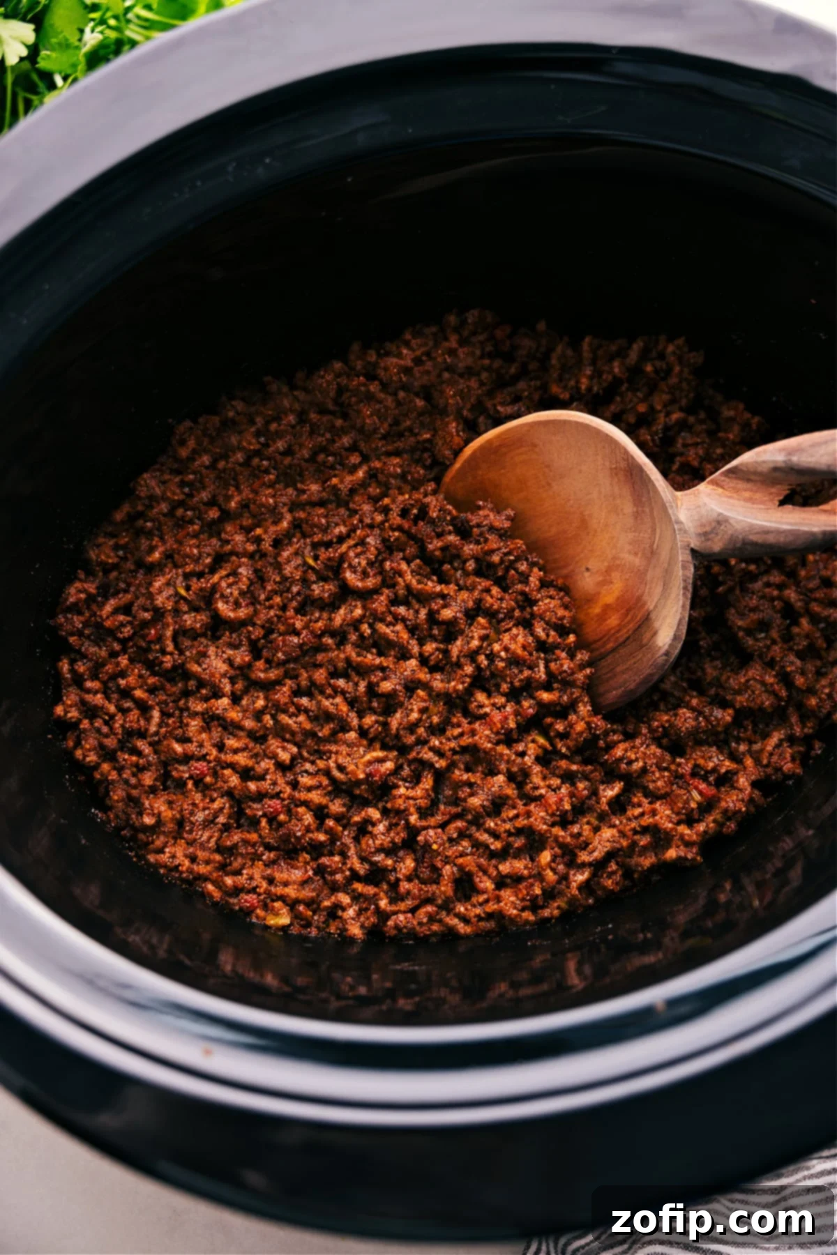 Crockpot Taco Meat simmering in a slow cooker, with a spoon lifting a portion of the savory beef, highlighting its rich texture and color.