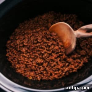 Appetizing Crockpot Taco Meat in a white bowl, ready for serving with various toppings in the background.