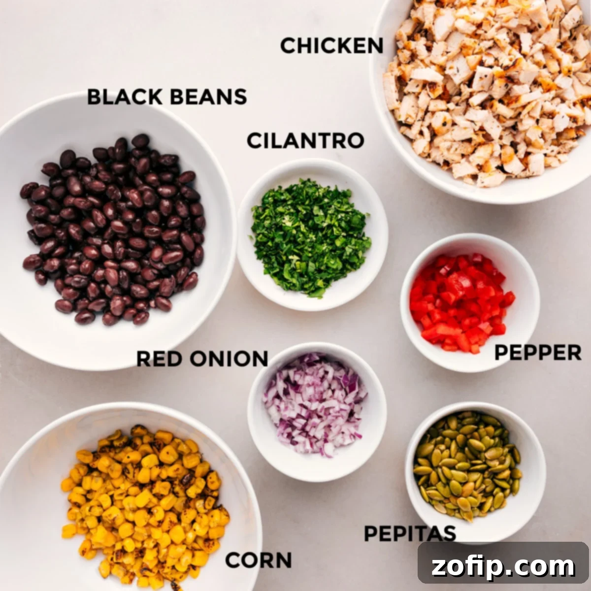 All the vibrant ingredients for Southwest Chicken Salad prepped and ready for easy assembly: cooked chicken, black beans, roasted corn, red bell pepper, red onion, cilantro, and pepitas.