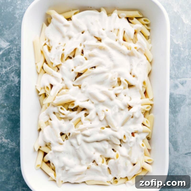 Adding White Sauce to Pasta Casserole - Preparing for Baking White sauce being poured over a casserole full of noodles, ready for baking.