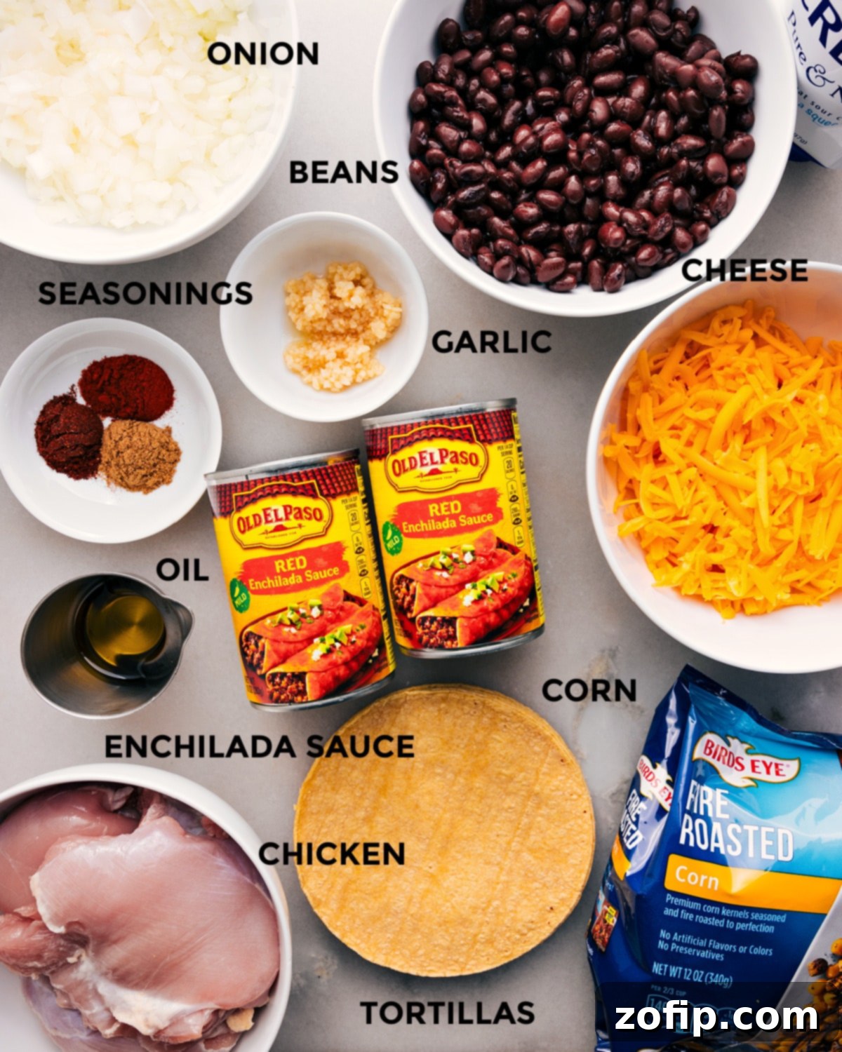 A colorful array of ingredients for Crockpot Chicken Enchilada Casserole, including chicken, enchilada sauce, corn tortillas, black beans, corn, cheese, sour cream, and spices, neatly arranged before assembly.