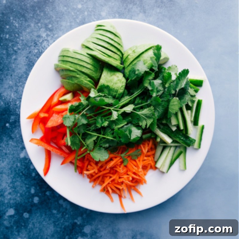 Overhead view of fresh, vibrant ingredients ready for Tuna Salad Wraps: neatly diced red bell pepper, shredded carrots, sliced cucumber, fresh cilantro, and creamy avocado slices.