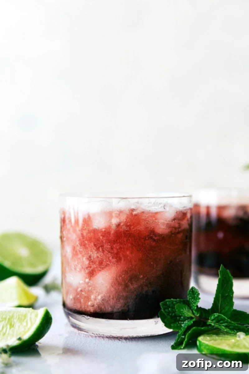 Close-up view of a vibrant red Tart Cherry Spritzer garnished with fresh lime and mint, inviting a refreshing sip.
