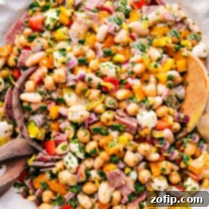 A close-up shot of the finished Dense Bean Salad in a bowl, showing the texture and vibrant colors of the beans, salami, cheese, and vegetables.