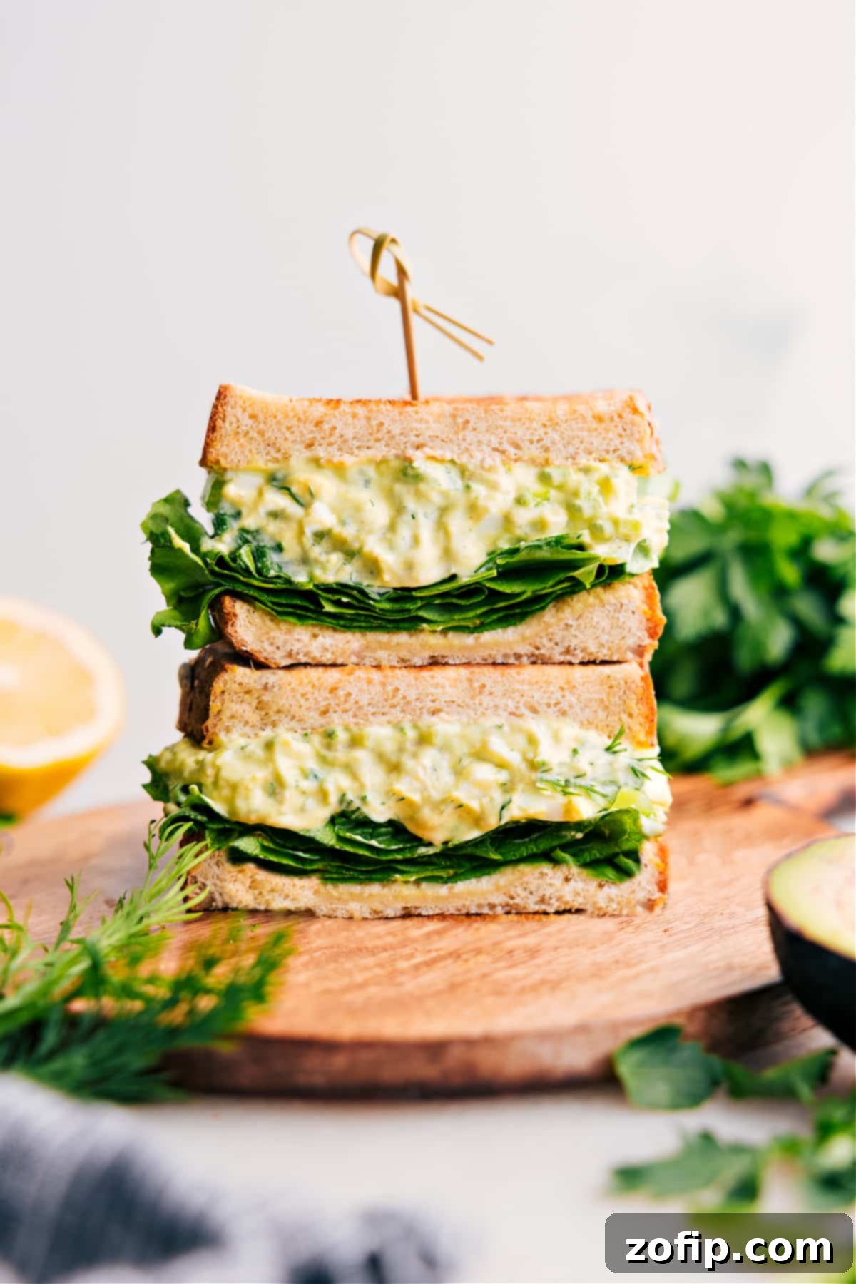 Avocado Egg Salad stacked high on toast, garnished with fresh herbs, ready to be enjoyed.