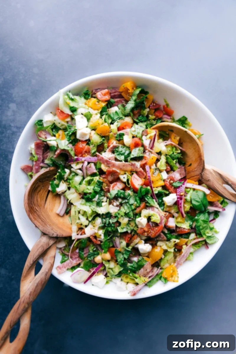 Colorful and vibrant Italian chopped salad with wooden serving spoons in the bowl, showcasing fresh ingredients.