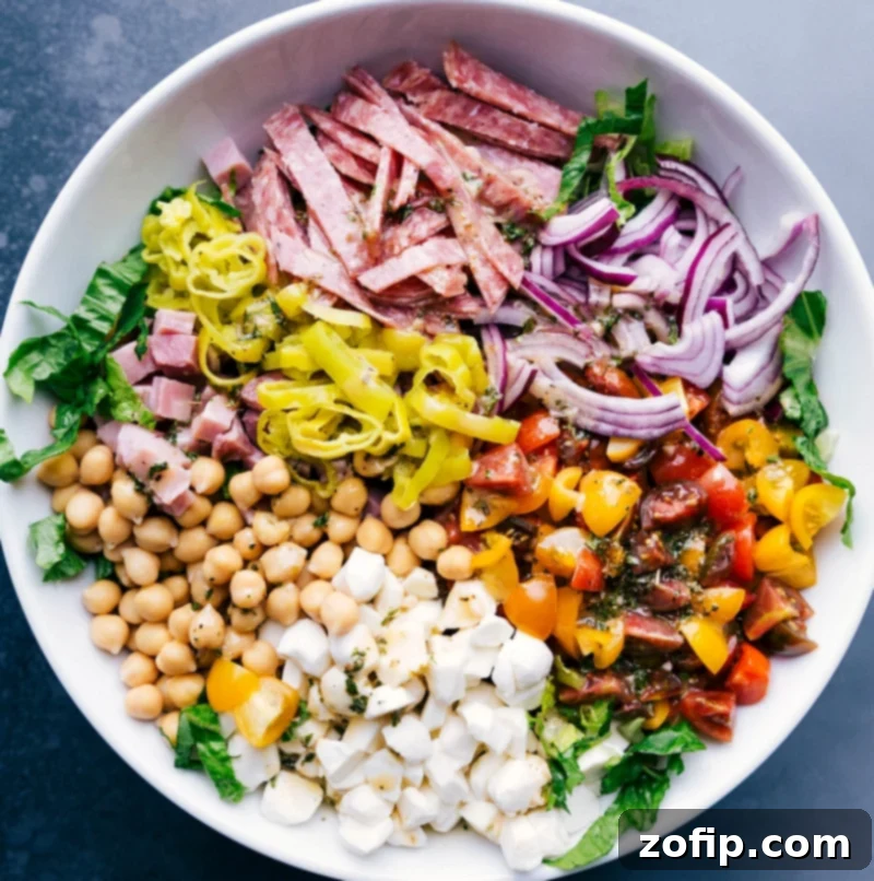 Salami, vibrant vegetables, and garbanzo beans meticulously layered over crisp lettuce, ready to be tossed.