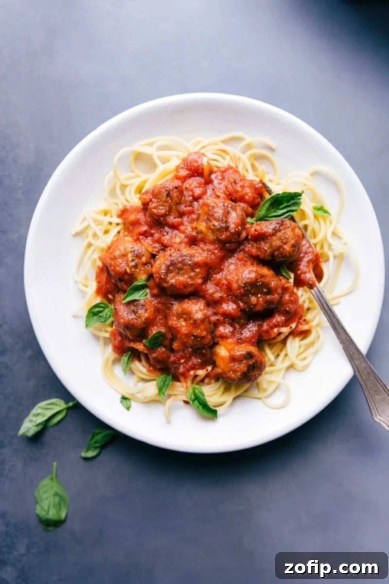 Chicken parmesan meatballs on a bed of pasta in a delicious red sauce, garnished with fresh herbs.