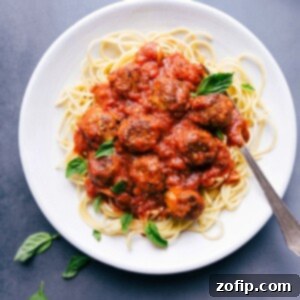 Chicken parmesan meatballs on a bed of pasta in a delicious red sauce, garnished with fresh herbs.