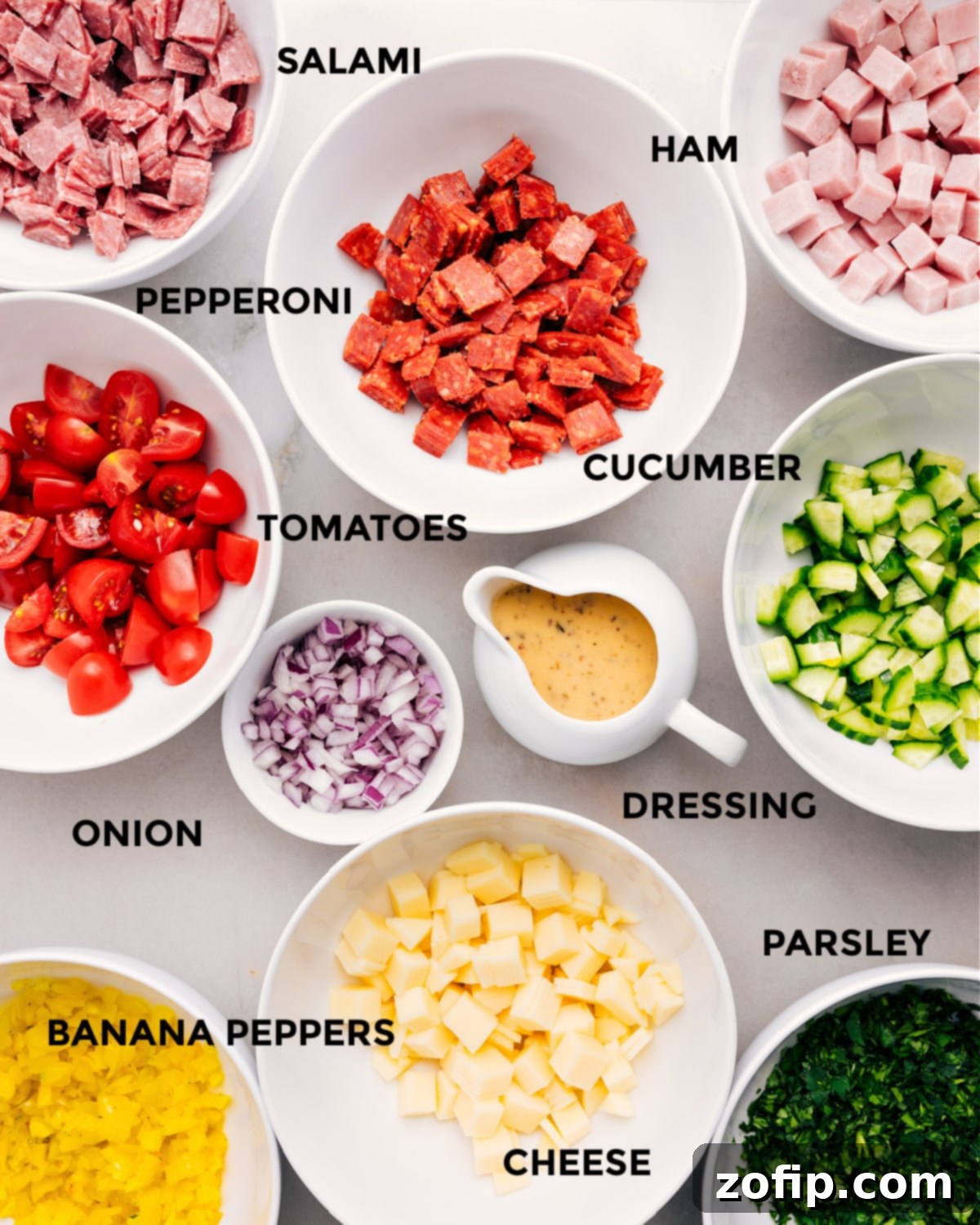 All the ingredients are prepped for easy assembly—meat, cucumber, tomatoes, onion, dressing, cheese, banana peppers, and parsley.