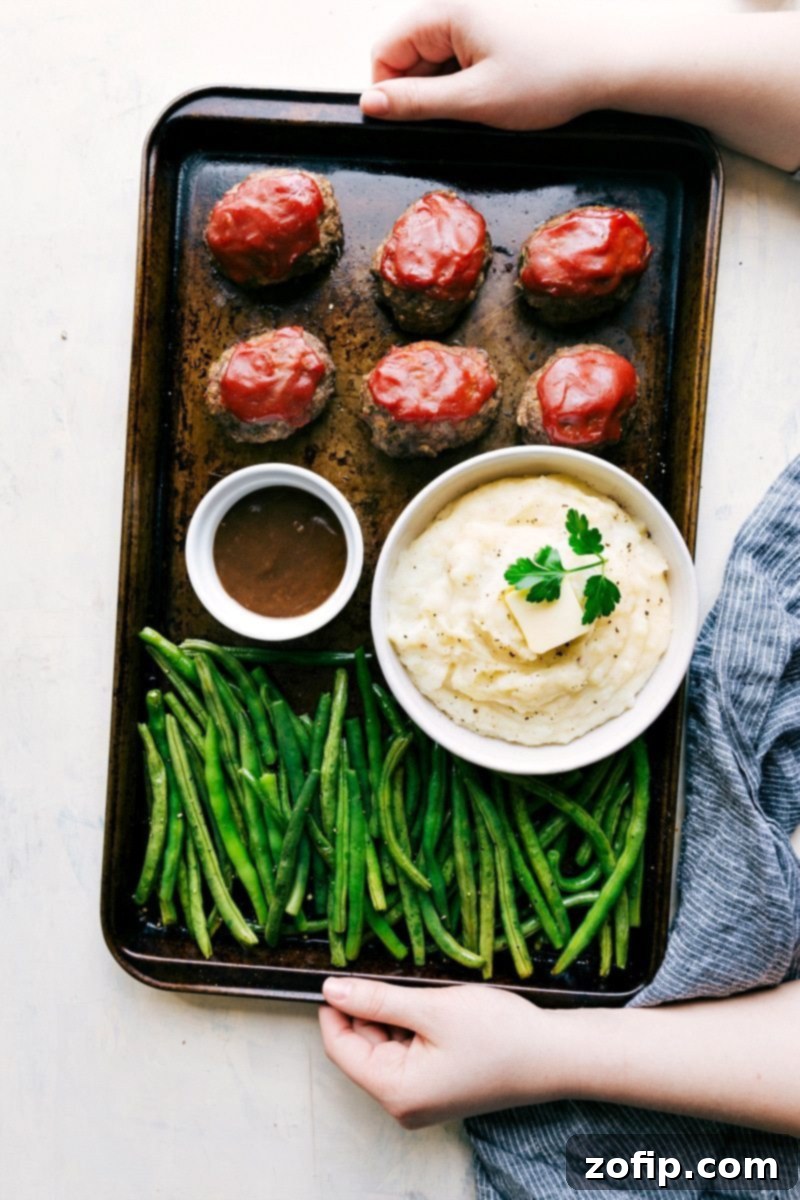 Overhead shot of the mini meatloaves all on one pan with potatoes, green beans, and gravy 