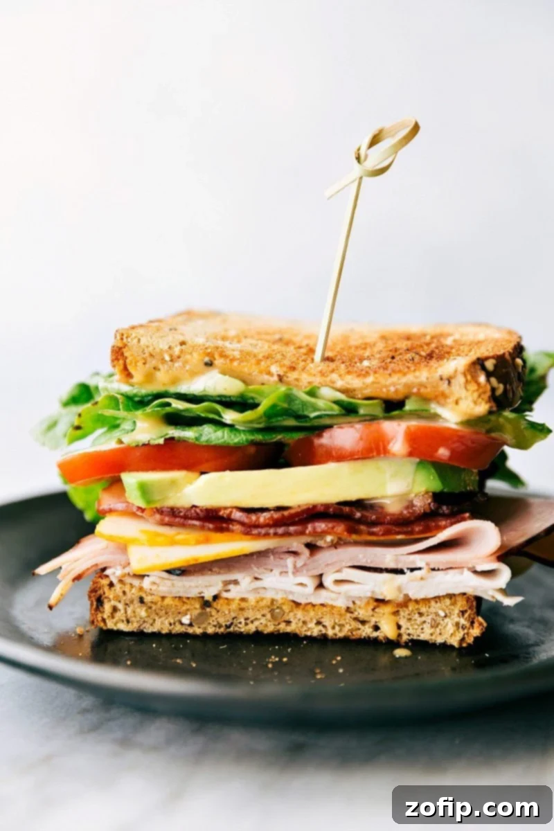 A perfectly assembled Honey Bacon Club Sandwich, showcasing layers of toasted bread, fresh greens, tomatoes, avocado, smoked turkey, honey ham, crispy bacon, and melted Muenster cheese, with a generous spread of honey mustard sauce.