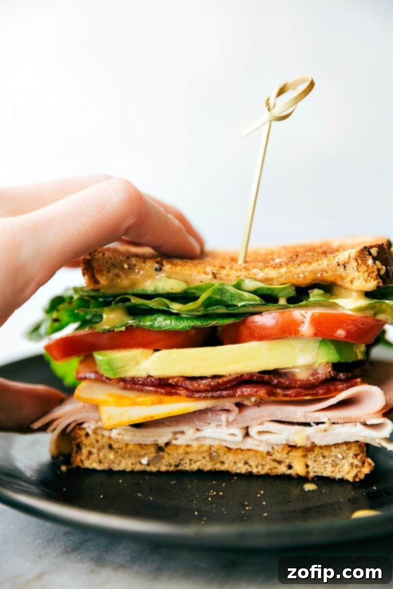 The finished Honey Bacon Club Sandwich, sliced in half and ready to serve, revealing its perfectly layered fillings and the golden toasted bread, with a side of extra honey mustard dipping sauce.