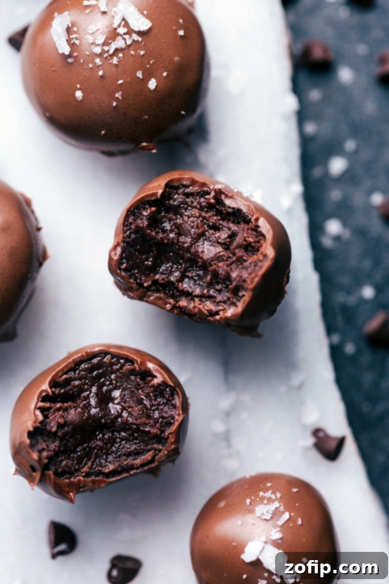 No-Bake Brownie Bites are rich, deeply fudgy, and completely indulgent! The soft, truffle-like filling is dipped in melted chocolate and optionally sprinkled in sea salt. Recipe via ChelseasMessyApron #dessert #best #quick #easy #simple #chocolatechip #seasalt #nobake #brownie #bites Perfectly dipped No-Bake Brownie Bites with a sprinkle of sea salt, ready for a delicious treat.