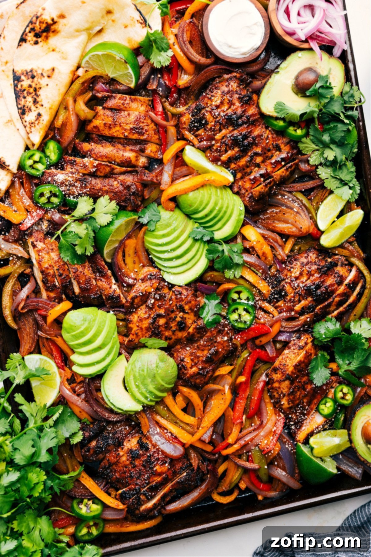 Sheet Pan Chicken Fajitas on the pan topped with fresh avocado, jalapeños, and cilantro.
