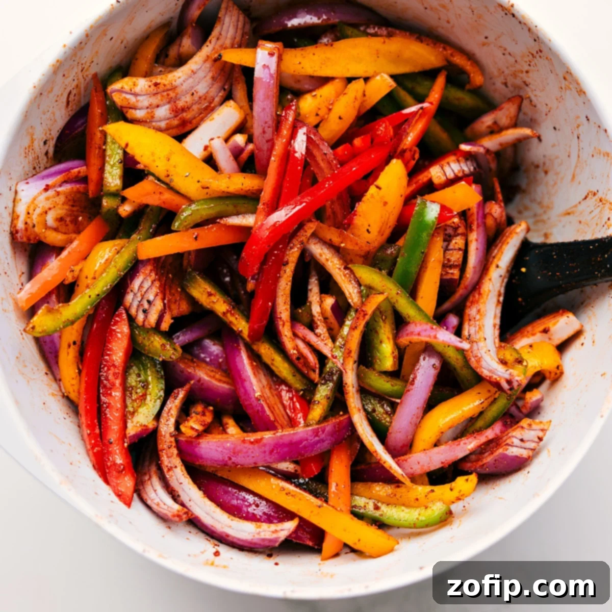 All the veggies chopped and tossed with the seasoning mix in a bowl for these sheet pan chicken fajitas.