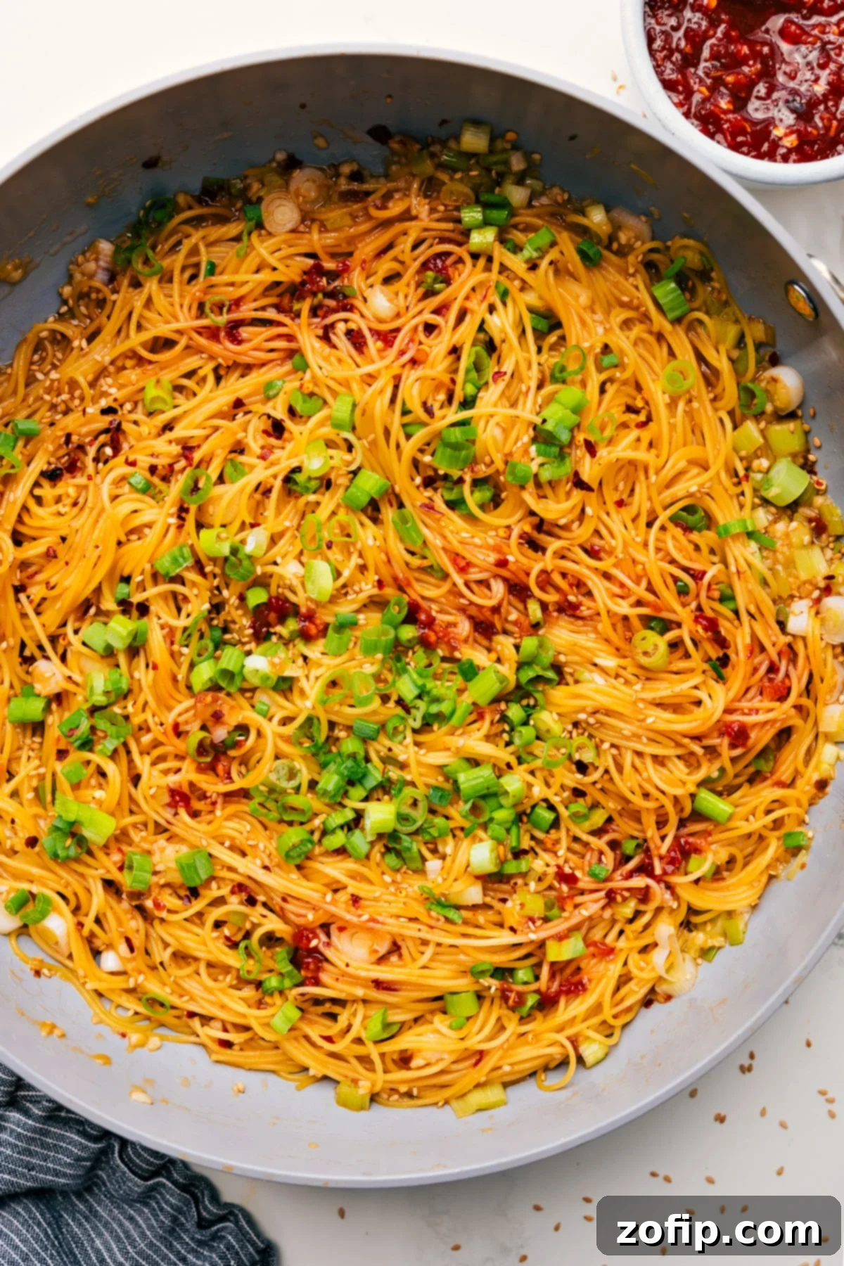 Chili Garlic Noodles in a skillet, garnished with green onions and sesame seeds.