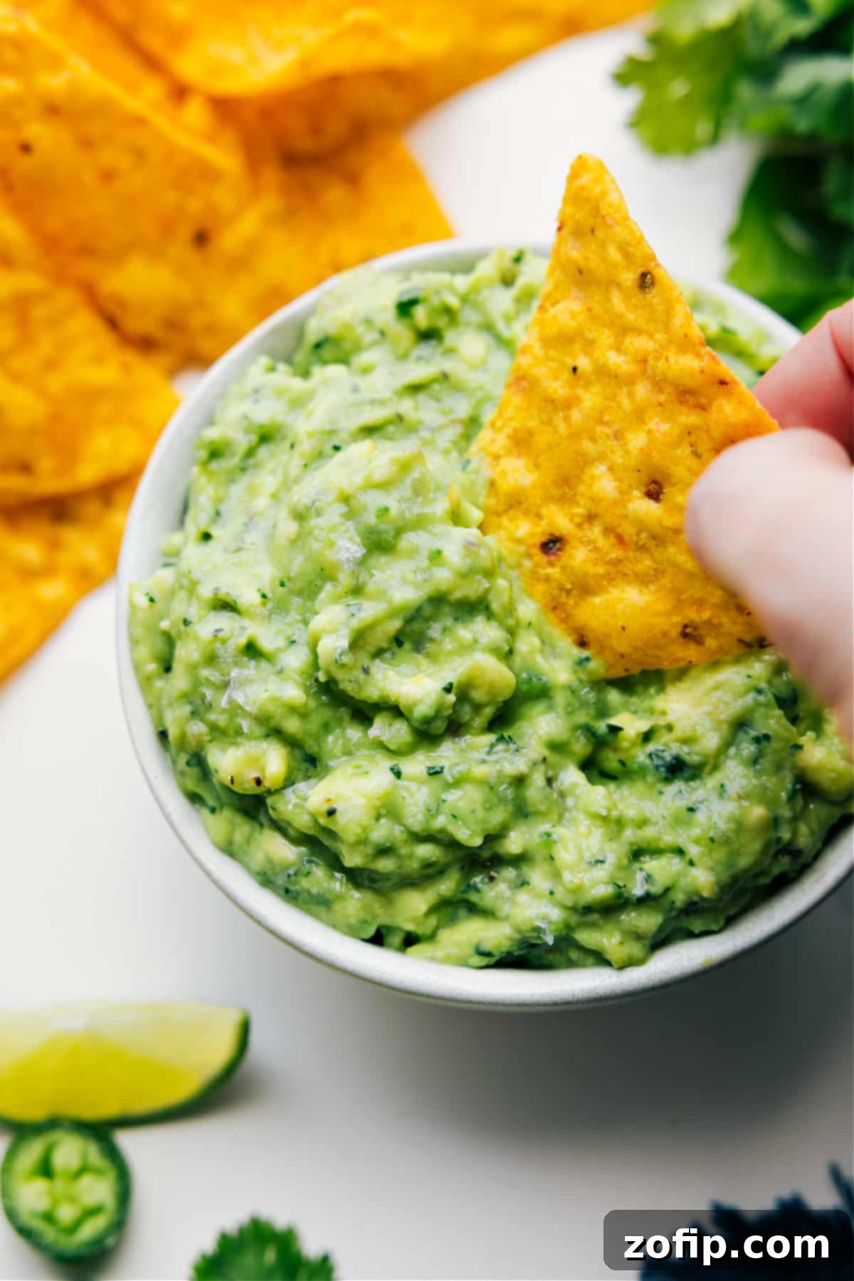 The Best Guacamole Recipe Straight From Maui Creamy guacamole recipe in a bowl with a tortilla chip dipped in, garnished with fresh cilantro.
