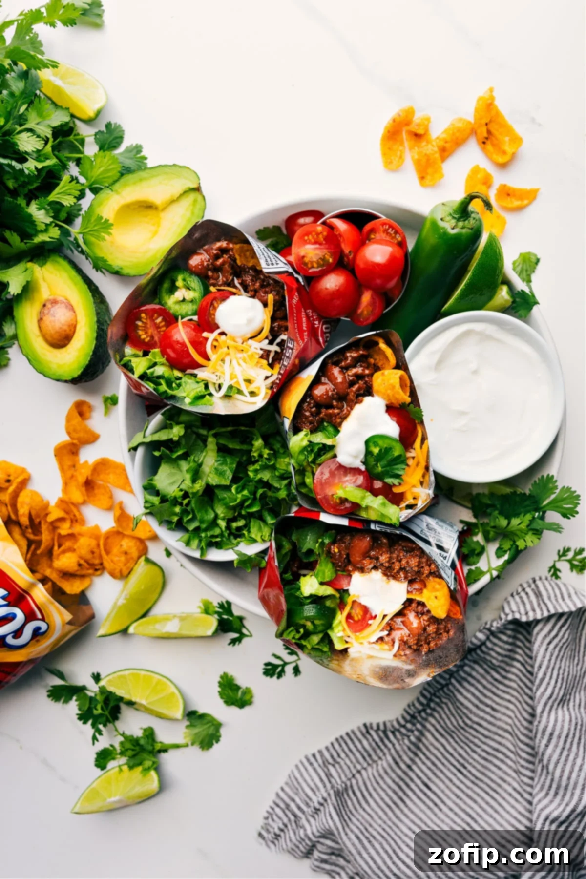 Walking Taco Recipe served on a plate with three chip bags filled with saucy ground beef, sour cream, tomatoes, lettuce, and jalapeños.
