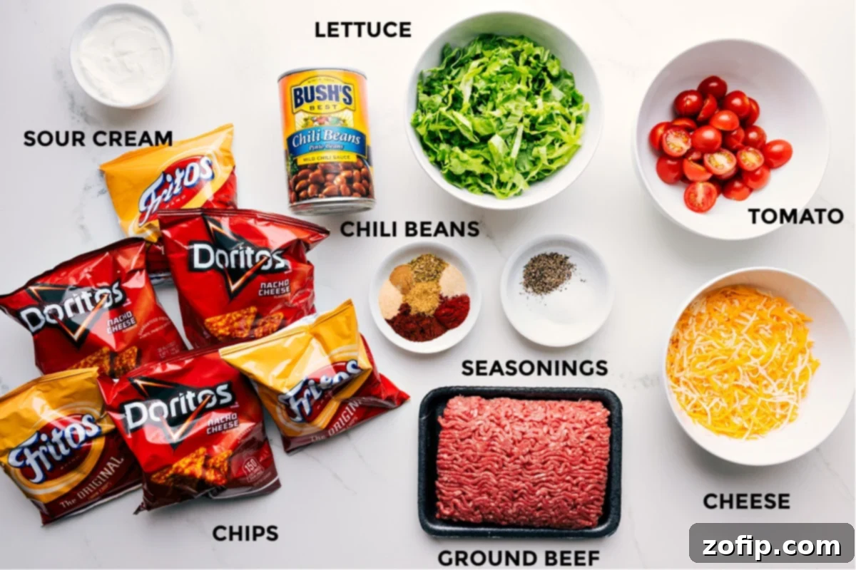 Ingredients in this recipe prepped for easy assembly, including sour cream, chili beans, lettuce, tomato, cheese, seasonings, ground beef, and chips.